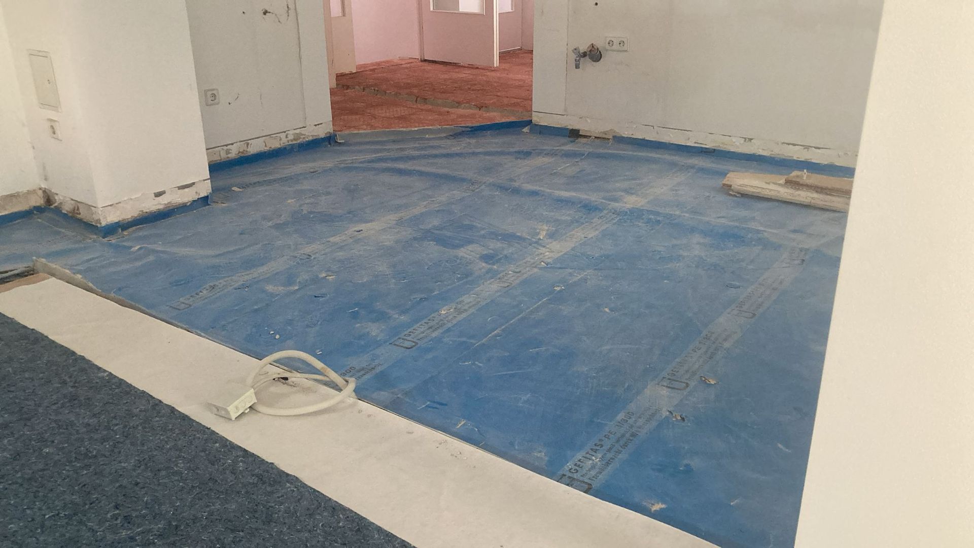 Blue-floored room under construction with white pillars, doorway, and debris. White trim on the floor.