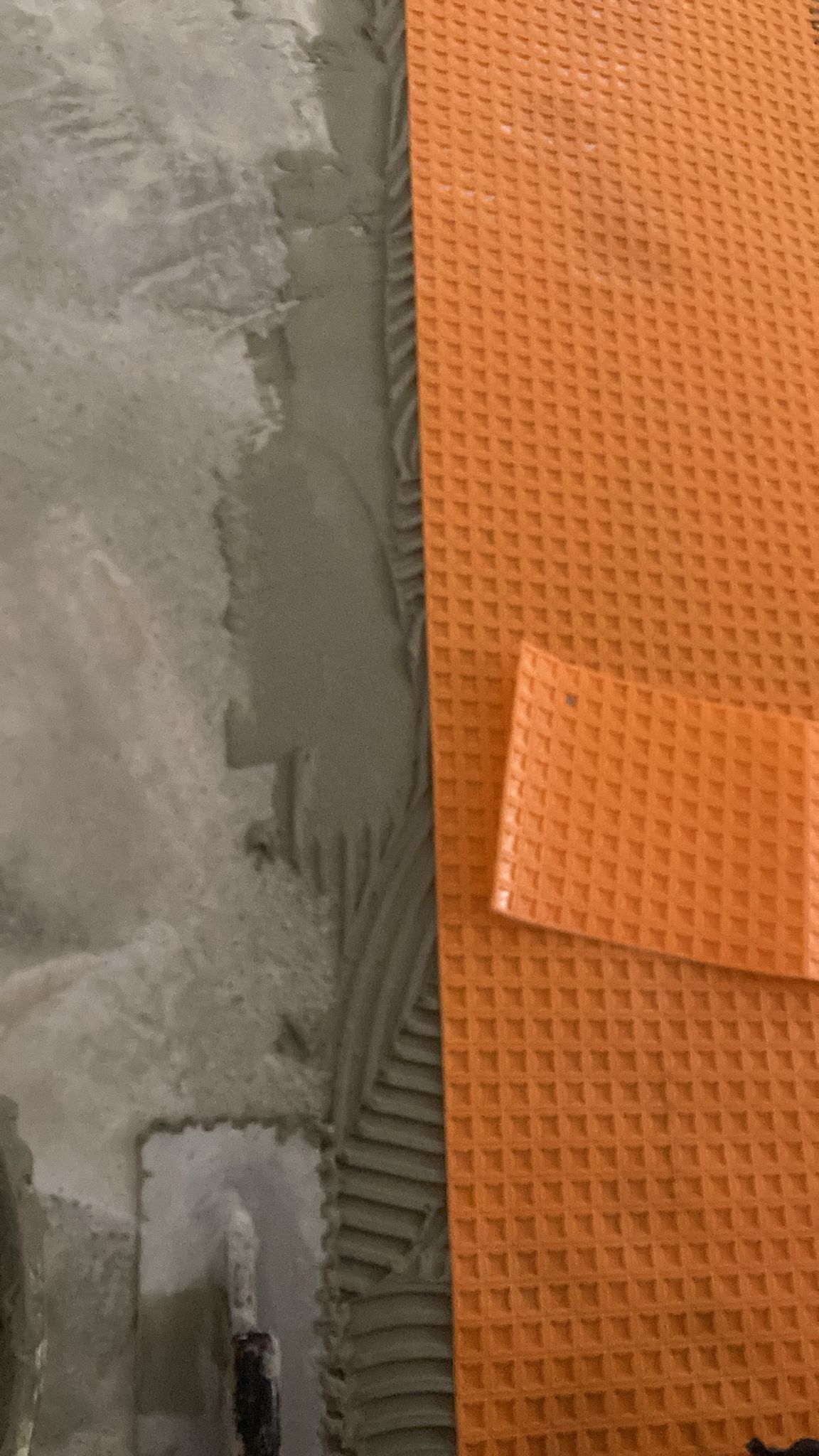 Orange tile membrane being installed on a concrete floor with mortar.