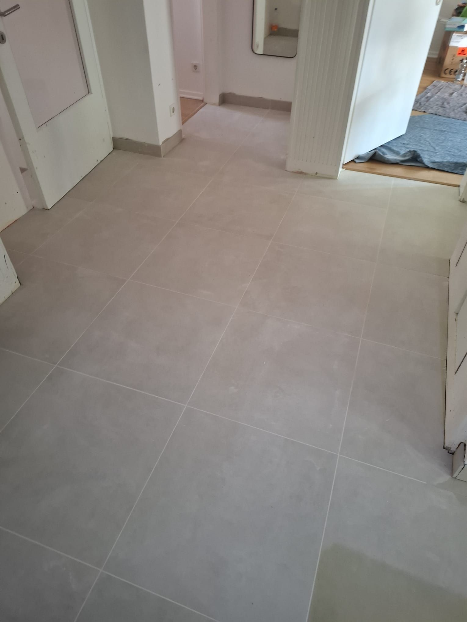 Gray tiled floor in a hallway with white walls and a door.