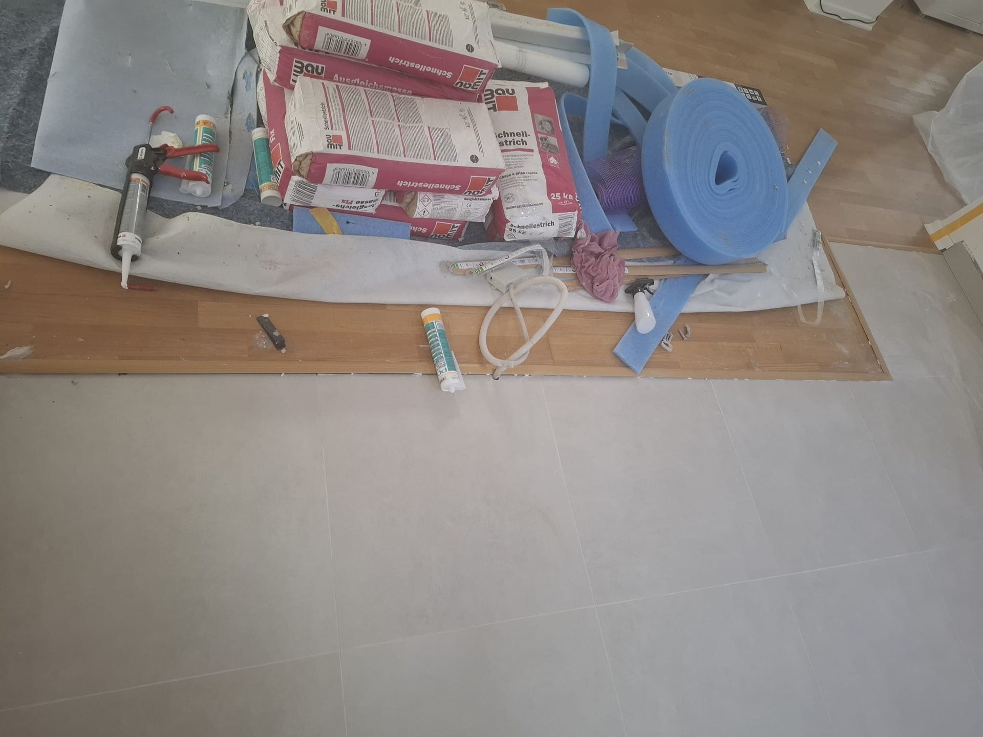 Construction materials on wooden floor: boxes, glue, blue foam roll, and white covering.