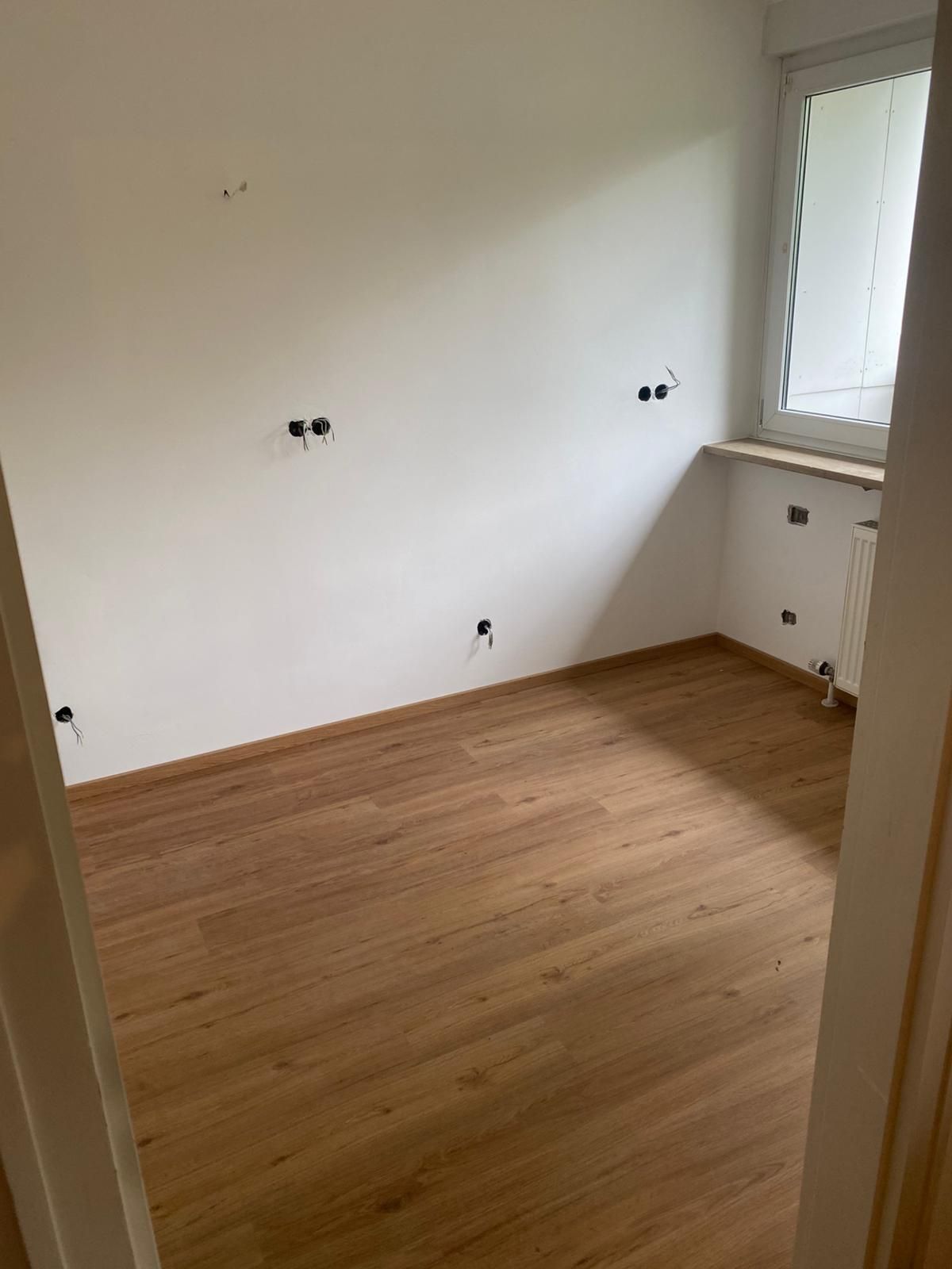Empty room with wood-look floor, white walls with electrical outlets, and a window.