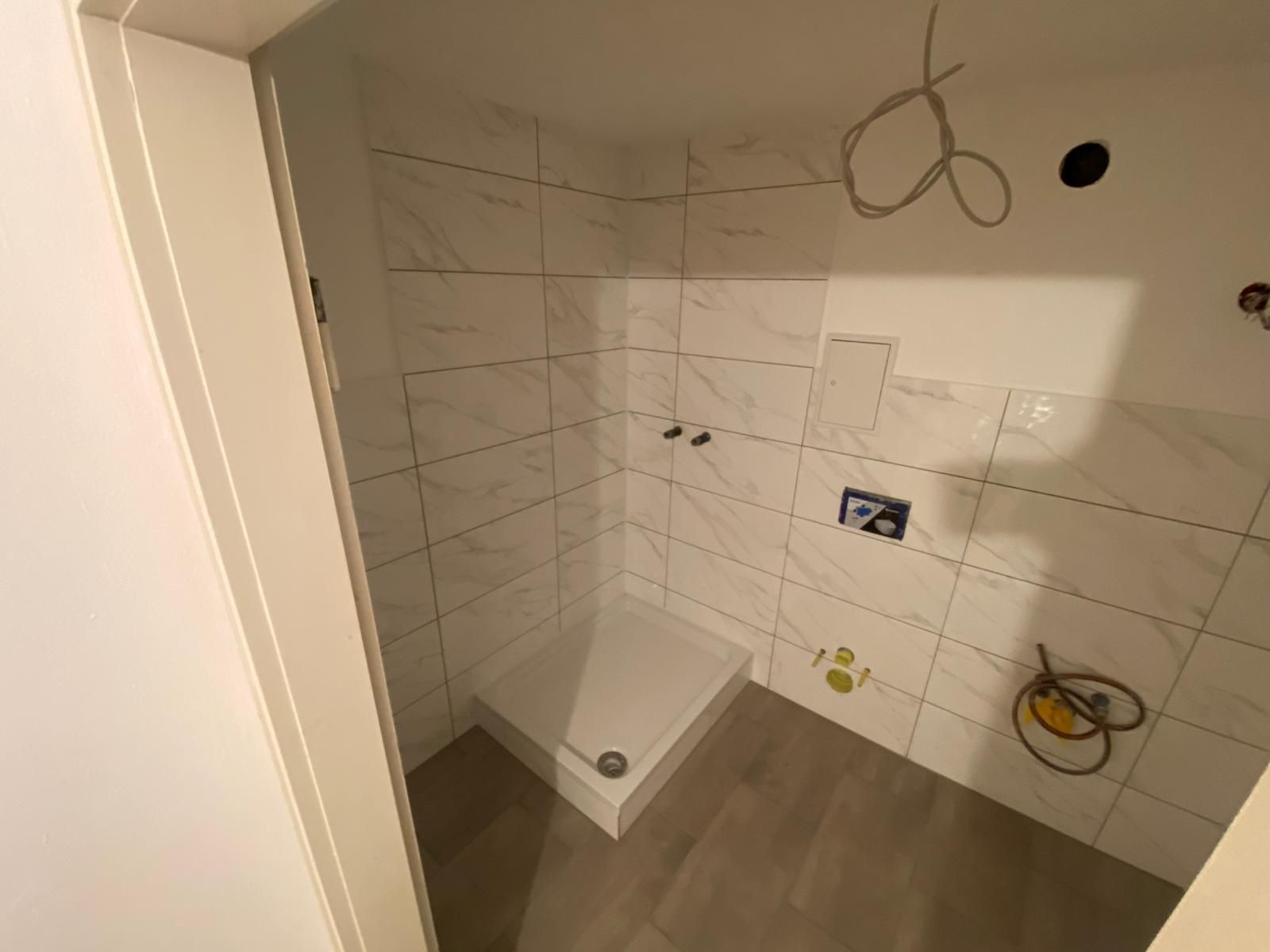 Newly tiled bathroom with shower stall, plumbing fixtures installed.