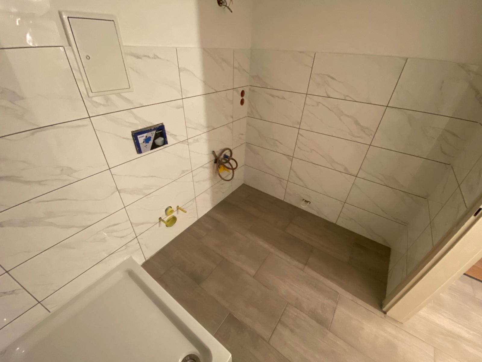 Bathroom with white marble-look tile walls, wood-look floor, and a white shower base; undergoing renovation.