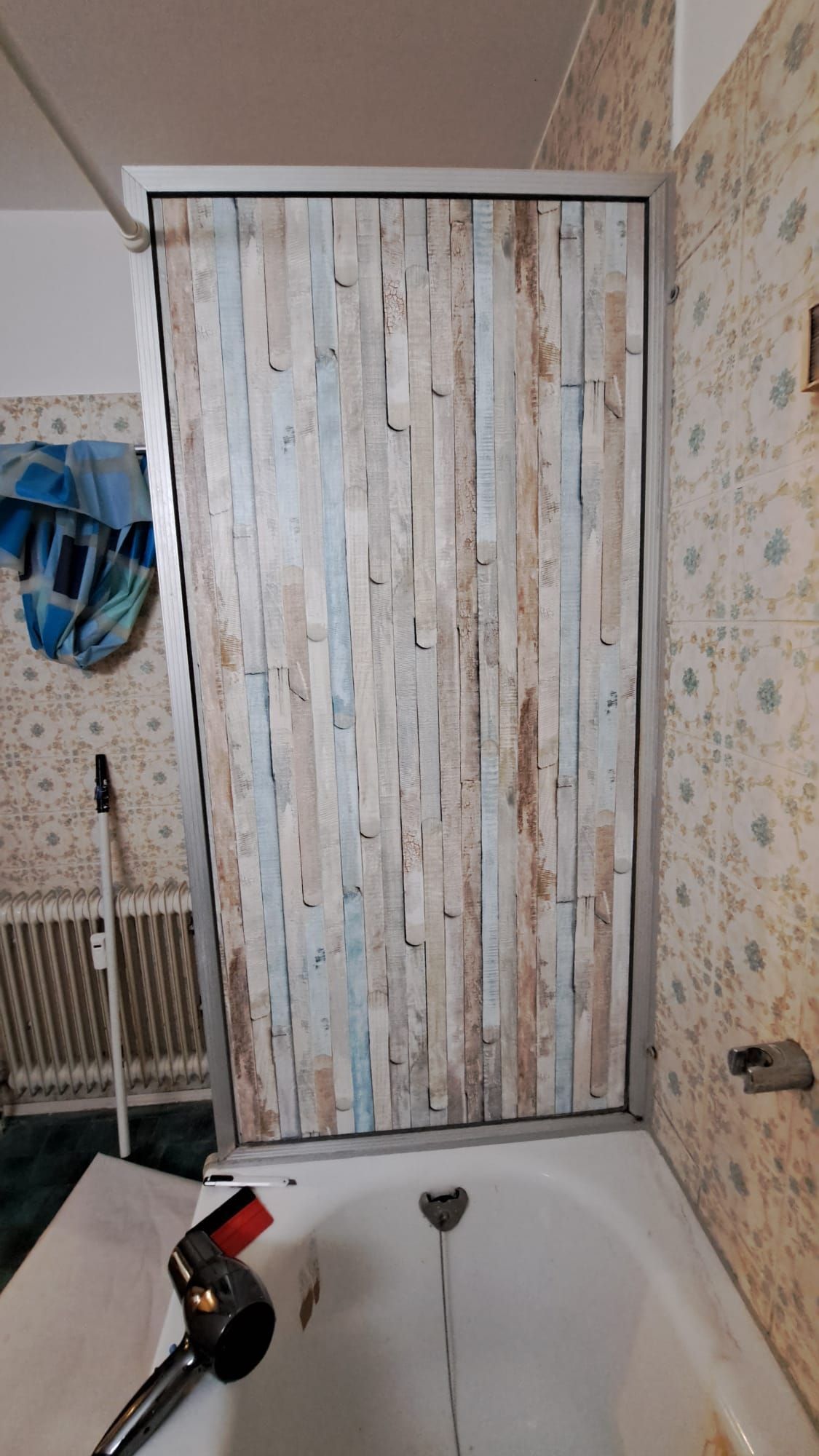 Shower door with a wooden plank pattern installed over a bathtub in a bathroom.
