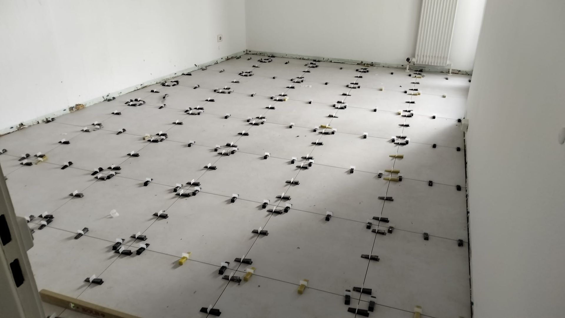 Floor with tiles installed, using leveling clips. Empty white room with light coming from a window.