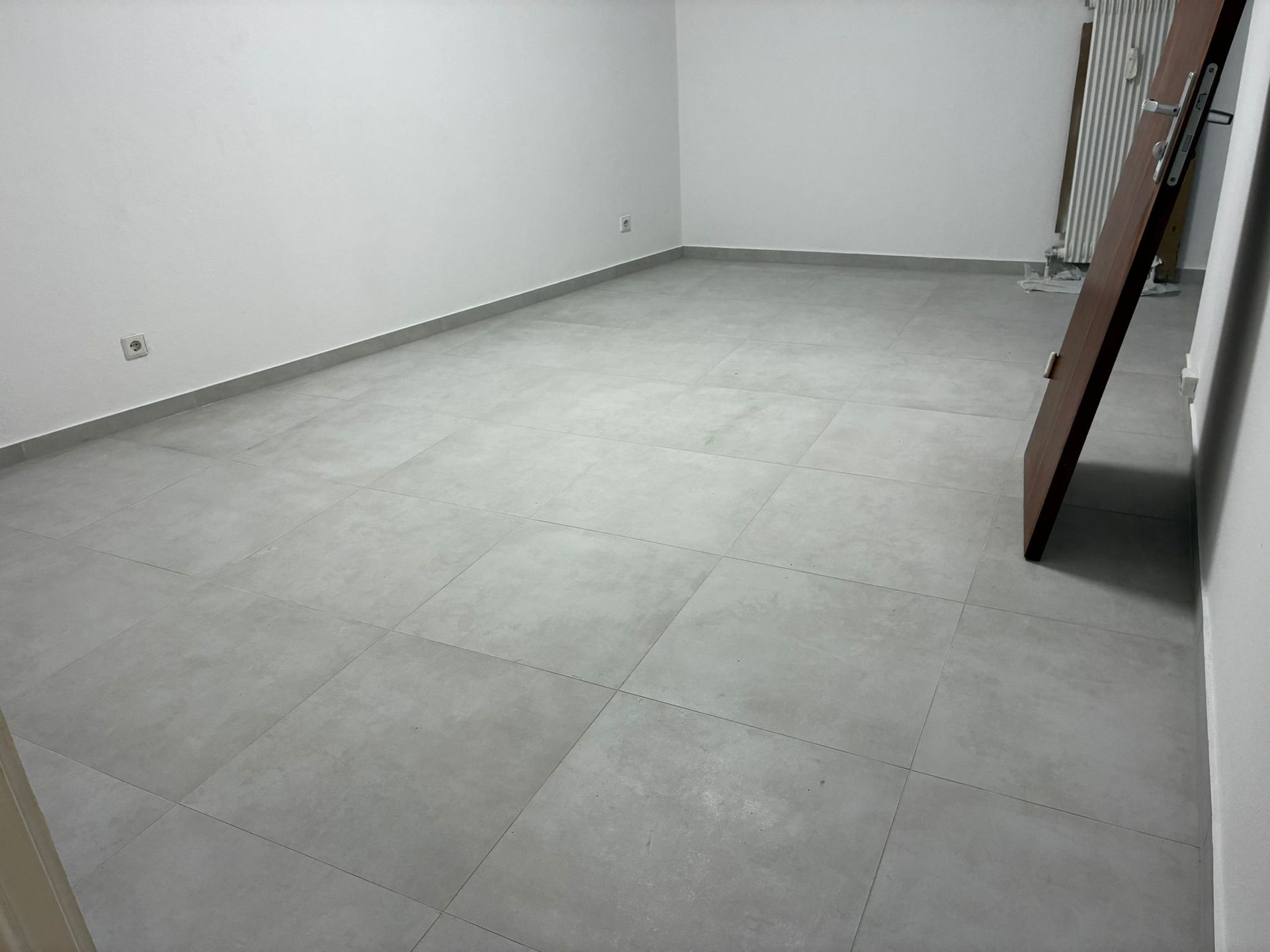 Empty room with gray tiled floor and white walls. A door and staircase are visible.