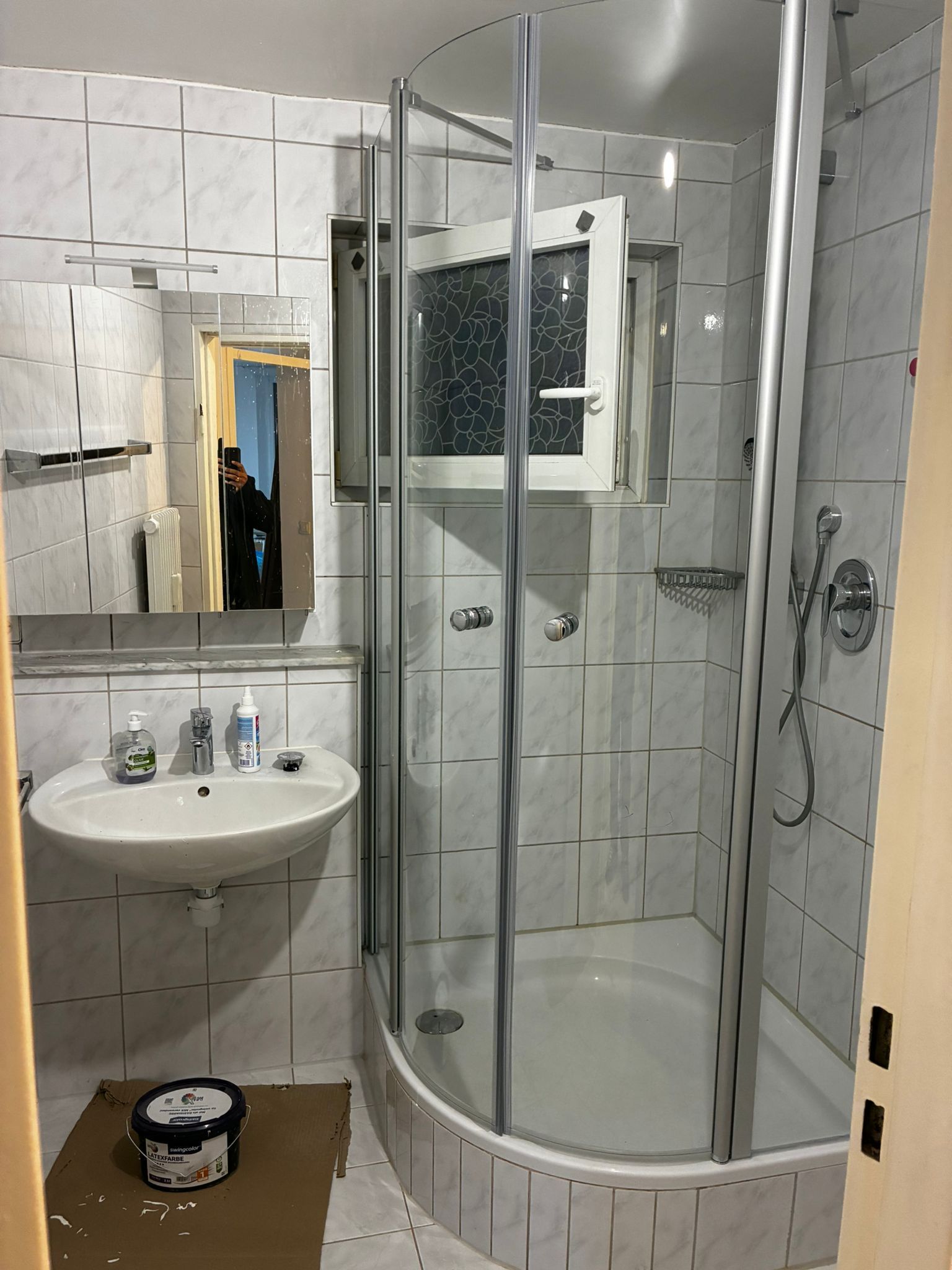 Small bathroom with a shower stall, sink, and window. Tiles are white.