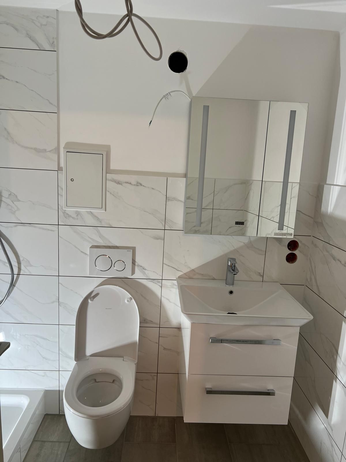 Bathroom with white tile, toilet, vanity with mirror, and electrical wiring.