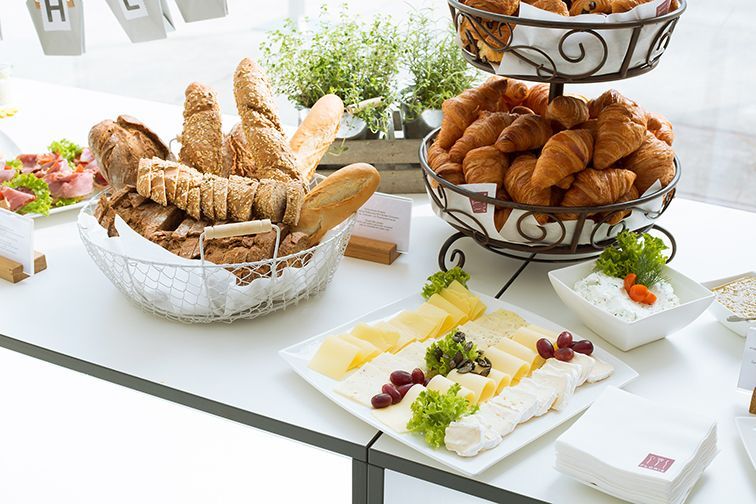 Ein reichhaltiges Frühstücksbuffet mit Körben voller Brotsorten und Croissants, einem Teller mit Käsescheiben und kleinen Beilagen.