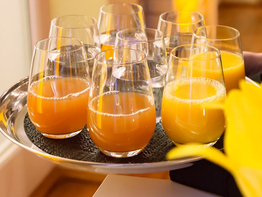 Menschen prosten sich zu. Hände halten Longdrinkgläser mit Cocktails und treffen sich mittig über einer Tischplatte