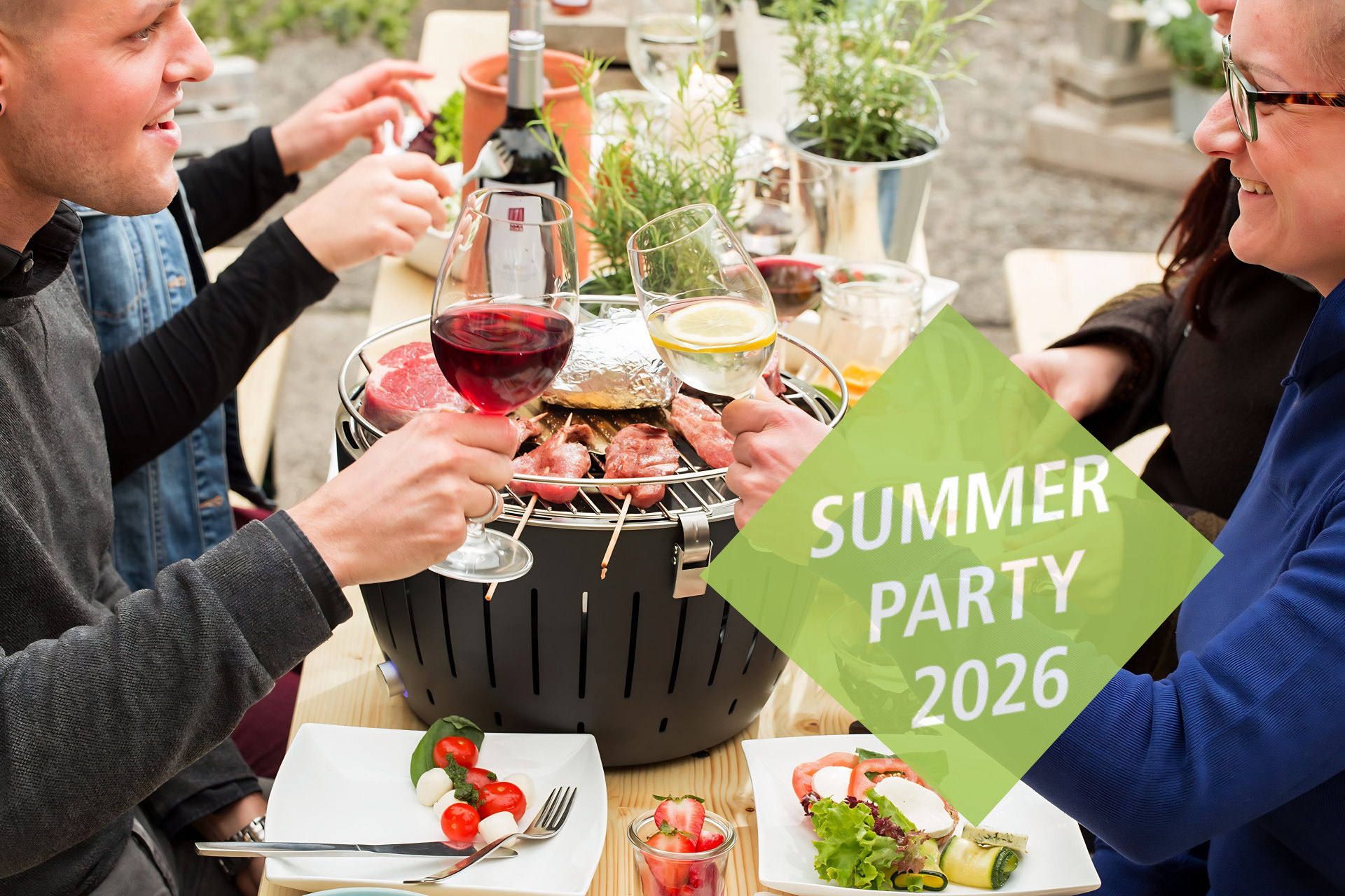 Menschen sitzen um einen Tischgrill und prosten sich z. Auf dem Grill Fleischspieße und Gemüse