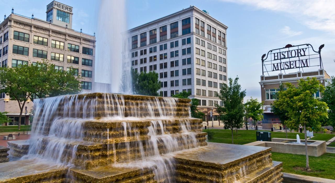 There is a waterfall in the middle of a park in front of a building.