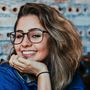 A woman wearing glasses is smiling with her hand on her chin.