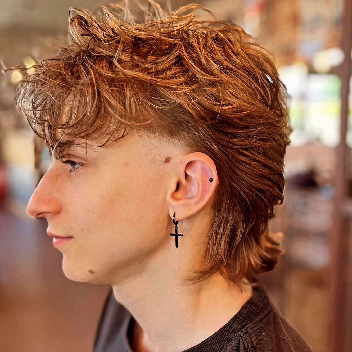 Persona con un moderno taglio di capelli mullet e piercing alle orecchie, che indossa una camicia scura.
