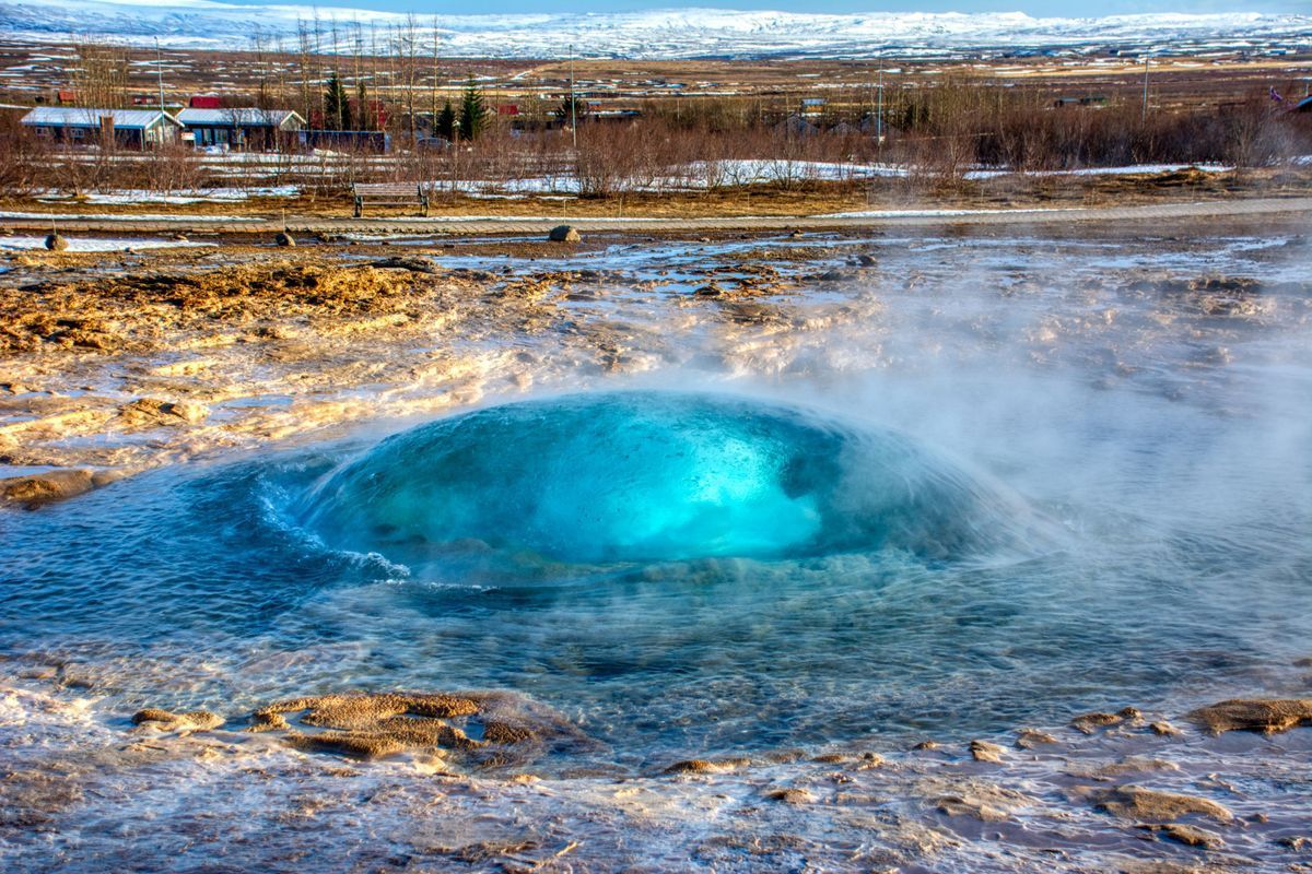 A bright blue bubble of water rises from a geothermal spring in a rocky, snow-dusted landscape.