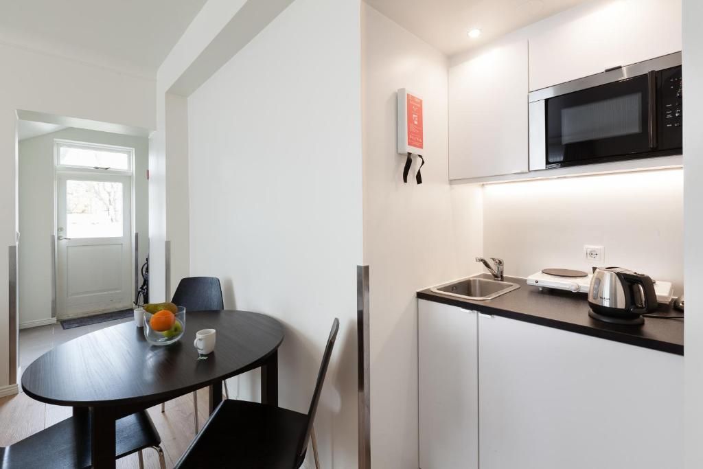 A compact kitchen area with a small, oval dining table, chairs, and a kitchenette featuring white cabinets and a microwave.