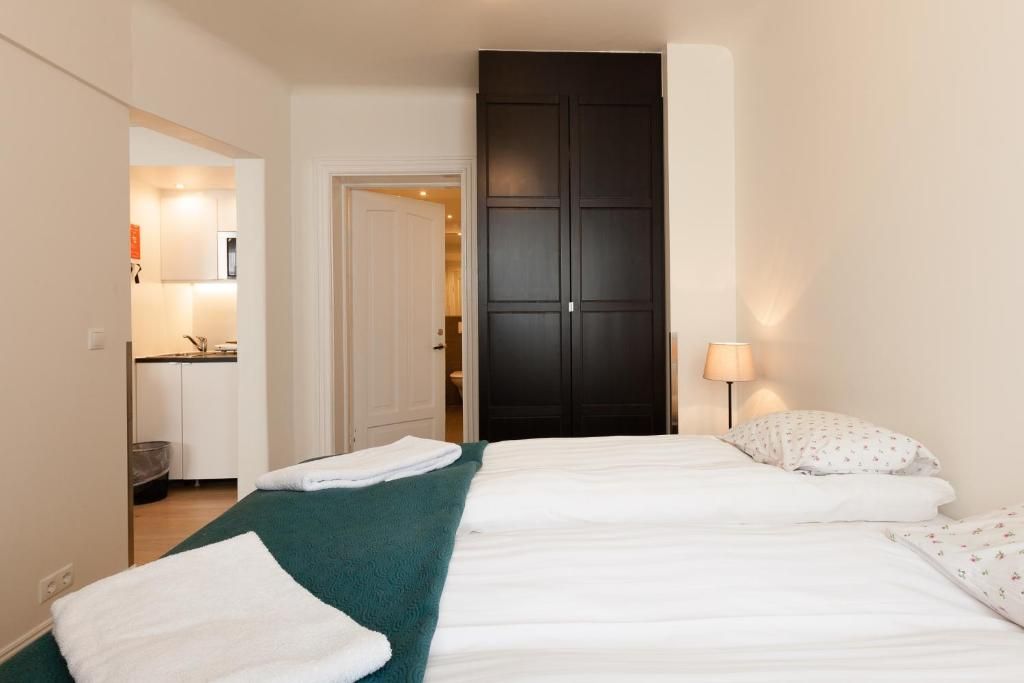 A hotel room view featuring two side-by-side beds with white linens, a dark brown wardrobe, and a small kitchen visible.
