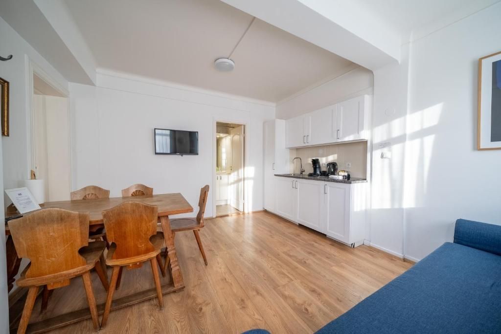 A minimalist apartment featuring a wooden dining set, a small kitchenette with white cabinets, and a blue sofa.
