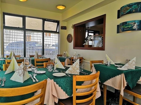 Tables set with green tablecloths and folded napkins in a dining room with large windows and wall decorations.