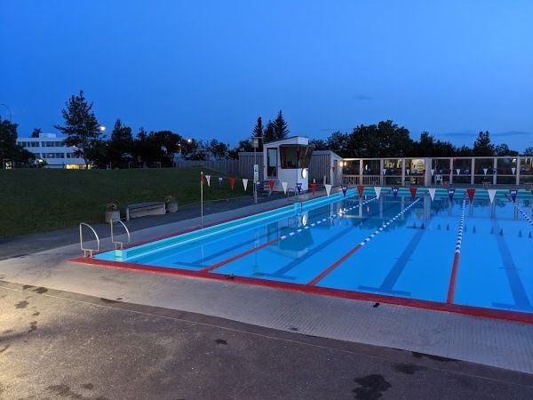 An outdoor lap pool with blue water and red lane markers at twilight, with a small lifeguard station in the background.