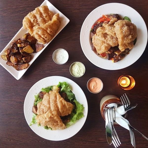 A flat lay of three plates featuring fried dough, roasted potatoes, salad, dipping sauces, and silverware on a table.