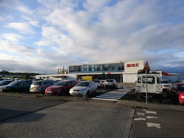 A low-angle view of the BSI bus terminal in Reykjavík, Iceland, with a parking lot in the foreground under a cloudy sky.