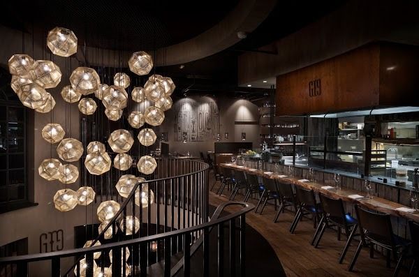 Upscale restaurant interior with a winding staircase, a long wooden bar, and an array of glowing, geometric pendant lights.