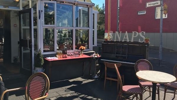 An outdoor cafe patio with a piano, cafe tables, chairs, and a red building in the background with the word 