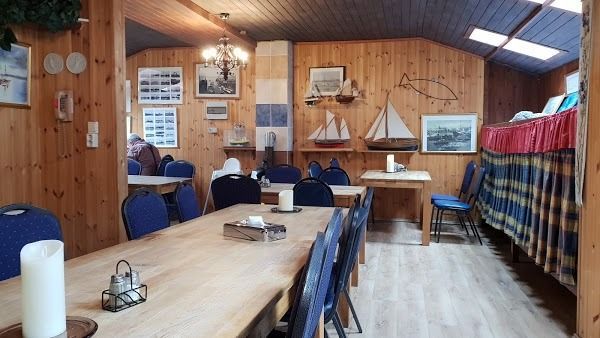 A dining area with wood-paneled walls, wooden tables, blue chairs, model sailboats, and nautical themed wall art.
