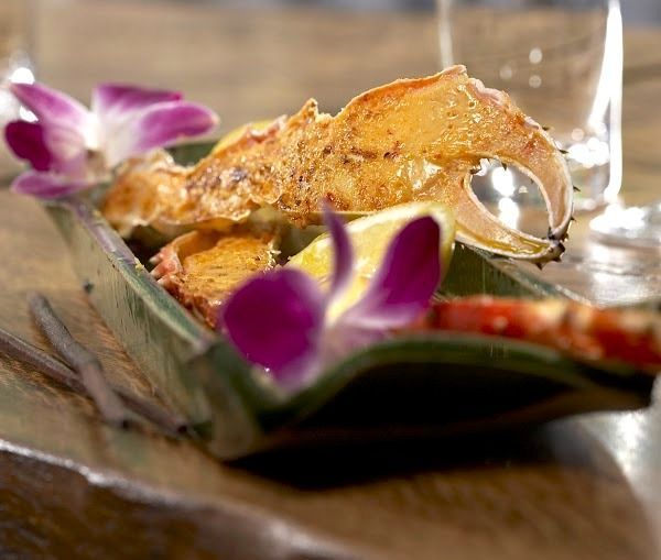 A plated crab claw garnished with purple orchid flowers and a lemon wedge on a wooden surface.