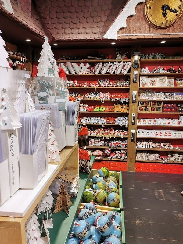A store shelf filled with Christmas ornaments, decorations, and gift items, with a wall clock visible at the top.