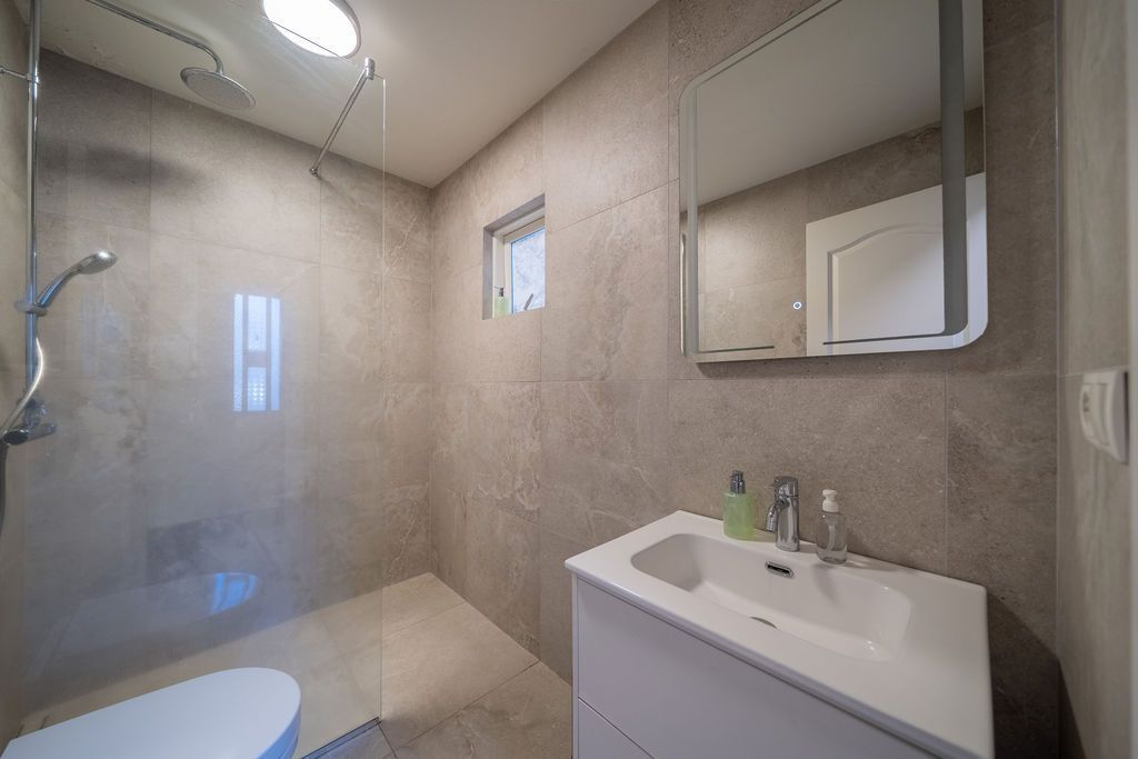 A modern bathroom with a glass-enclosed shower, a white vanity sink, a mirror, and neutral-toned tiled walls.