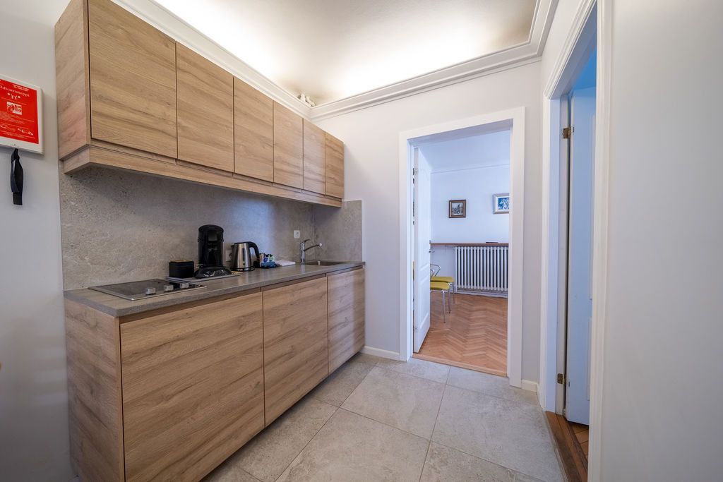 Small kitchen with light wood cabinets, granite countertops, and a doorway leading to a tiled room.