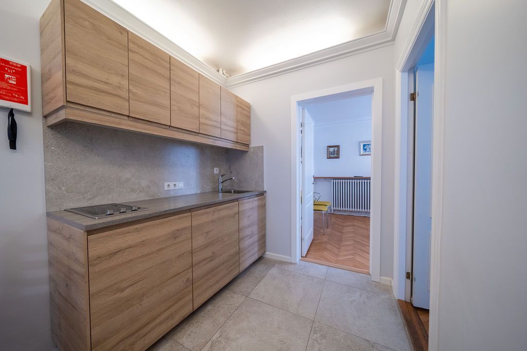A kitchenette with wood-grain cabinets and counters, featuring a stovetop and sink, next to a doorway to another room.
