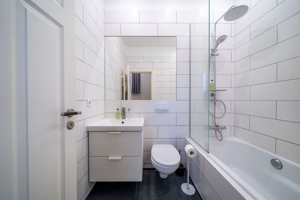 A modern bathroom with white subway-tiled walls, a floating vanity, a toilet, and a bathtub with a glass shower screen.