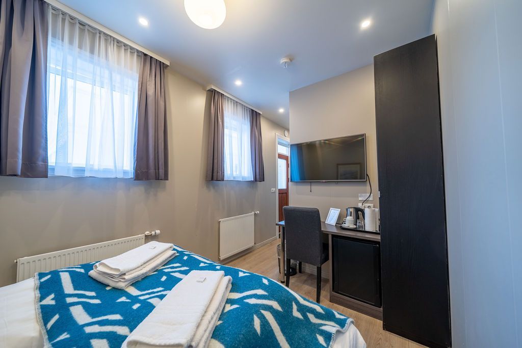 A hotel room with a bed featuring a blue and white patterned spread, a desk with a chair, and a mounted television.