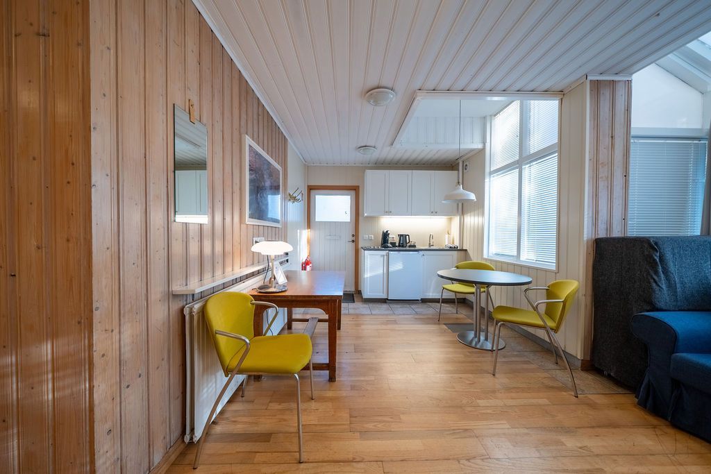 A well-lit, modern apartment interior with wooden walls, a small dining area, and a bright kitchen in the background.