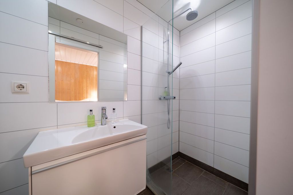 A modern bathroom featuring a white vanity with a basin, a mirror, and a walk-in shower with white tiled walls.