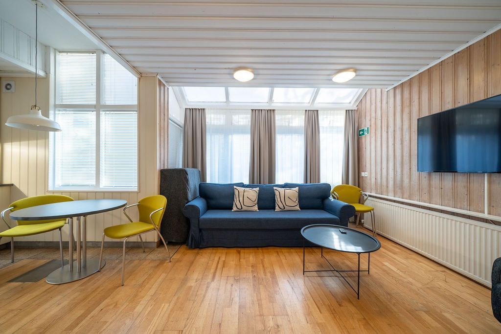 A bright living room with a blue sofa, coffee table, and dining area on hardwood floors, under a glass-paneled ceiling.