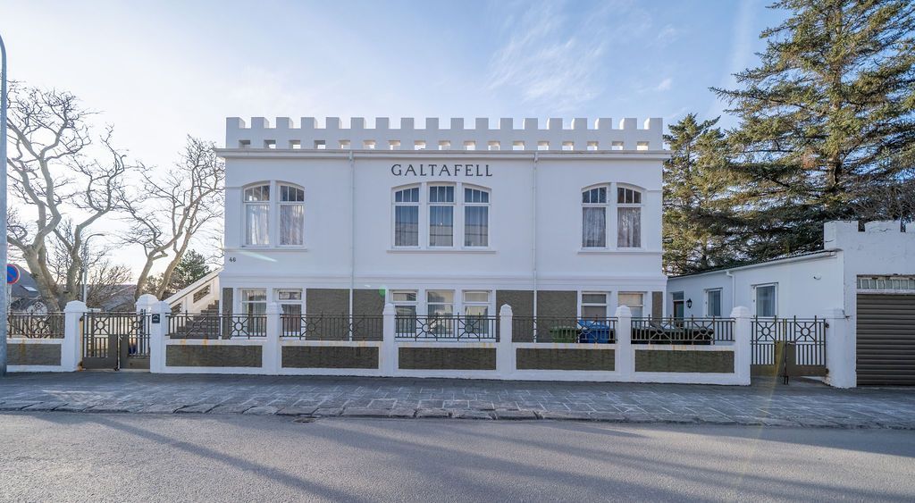 A white two-story building with battlement-style roof trim, set behind a low wall with iron gates, under a clear blue sky.