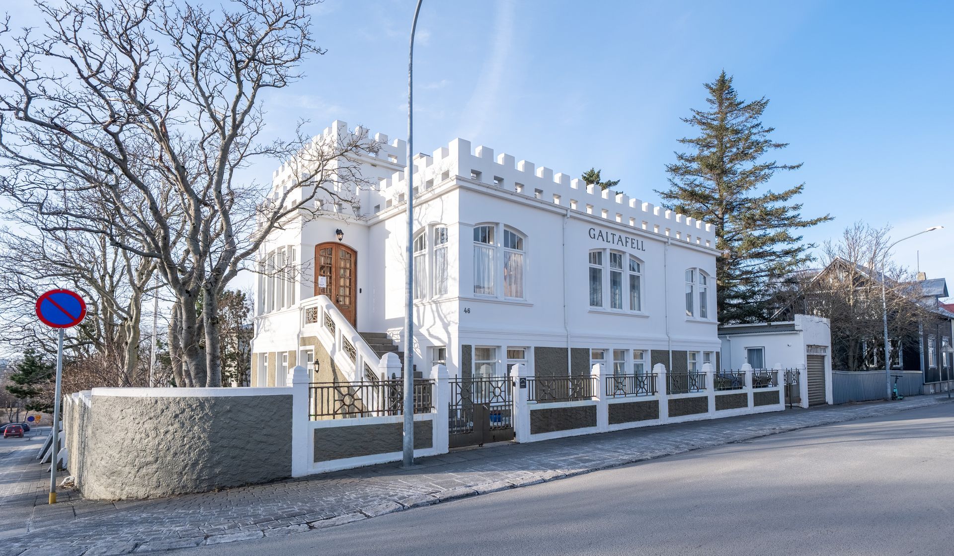 A white, castle-like house with a crenellated roofline, stone-textured base, and front staircase, set by a city street.