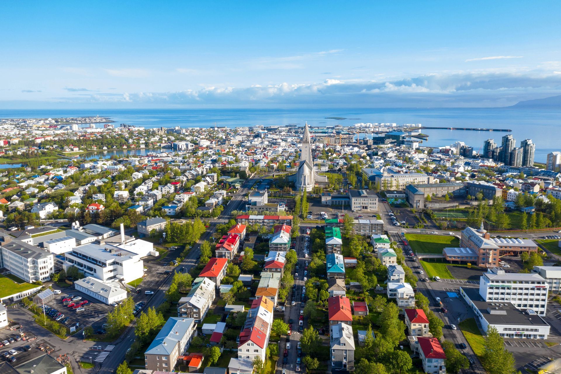 Aerial view of Reykjavik, Iceland, showing colorful houses, the Hallgrímskirkja church, and the harbor under a blue sky.