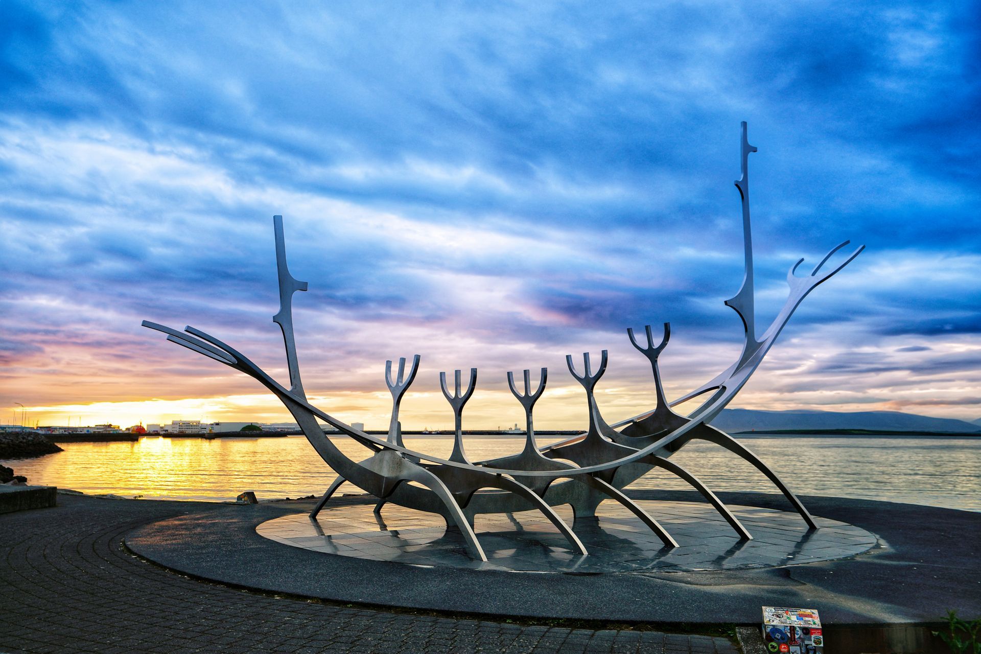 The Sun Voyager, a large steel Viking ship sculpture, stands on a rocky shore in Reykjavik, Iceland, against a sunset.