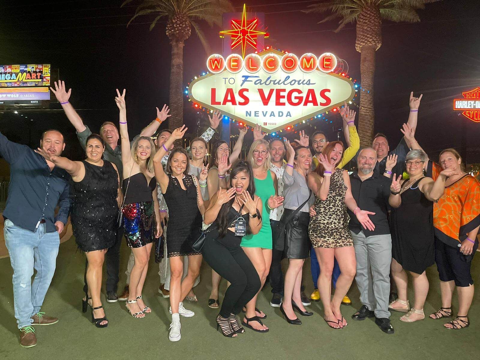Excited group of friends celebrating at night in front of the famous 'Welcome to Fabulous Las Vegas, Nevada' sign and capturing the ultimate Vegas nightlife experience.