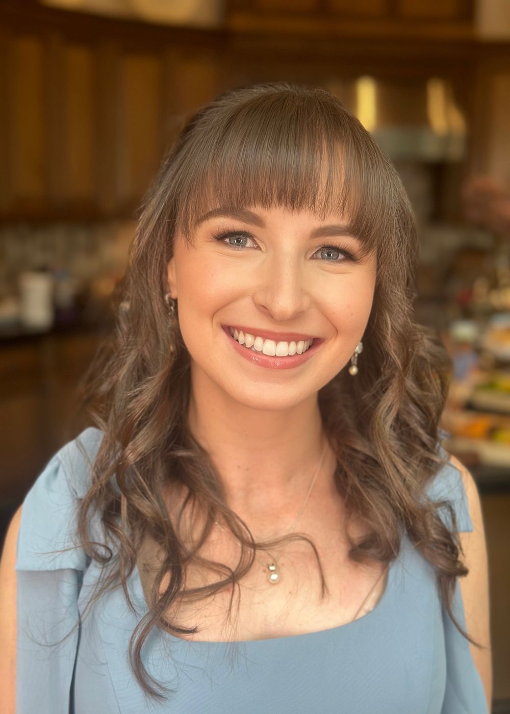 Smiling woman in a blue top indoors with softly blurred warm background