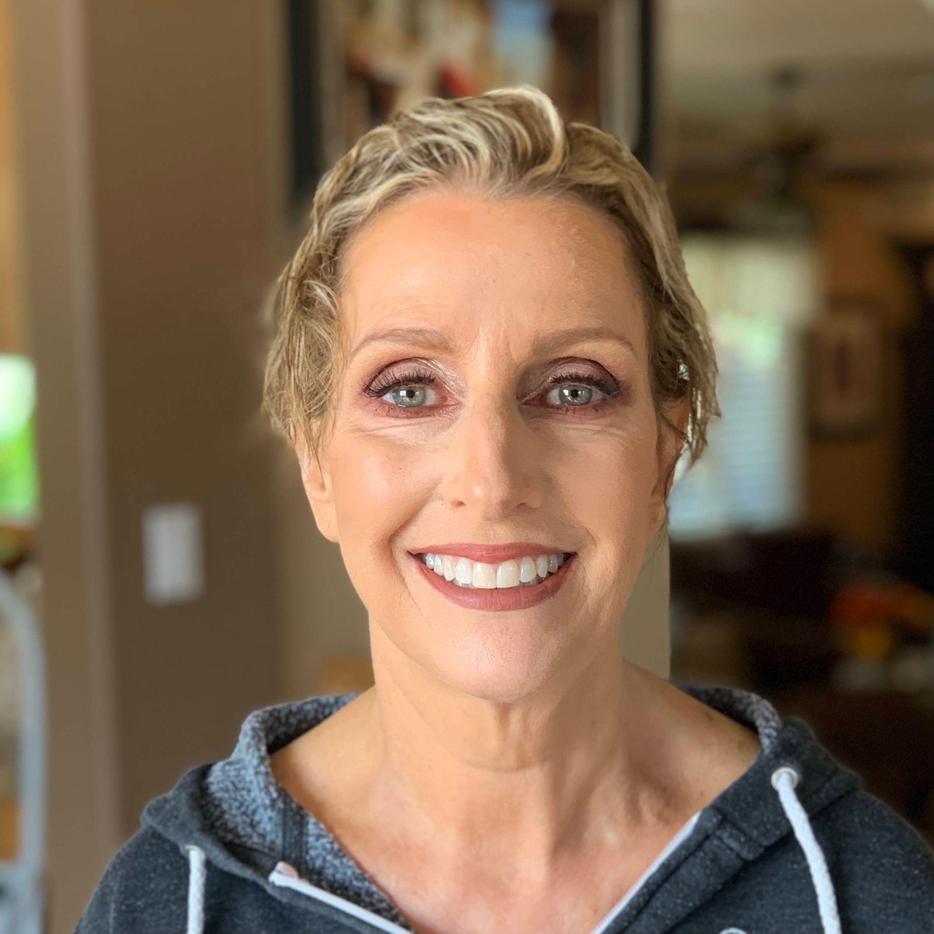 Smiling woman in a gray hoodie indoors with a softly blurred background