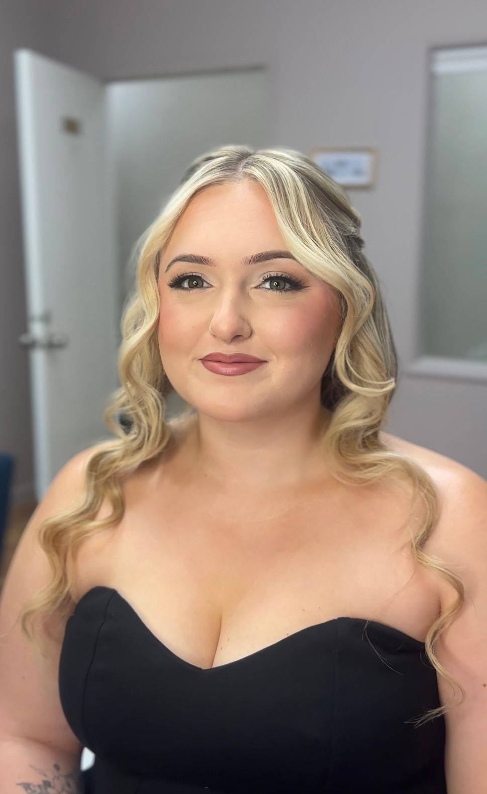 Woman in a black dress posing indoors against a softly lit hallway background