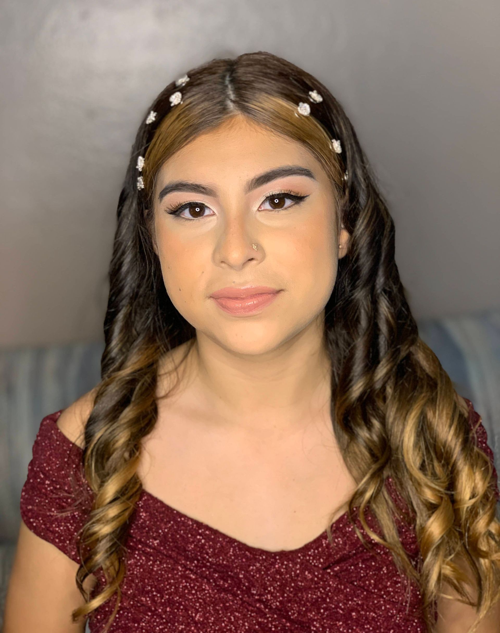 Person with long curled hair, sparkly hair clips, and maroon top against a gray background