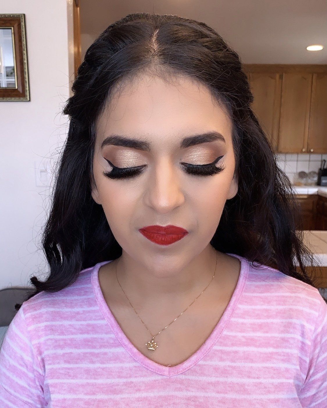 Woman with closed eyes, red lipstick, and pink shirt standing in a kitchen.