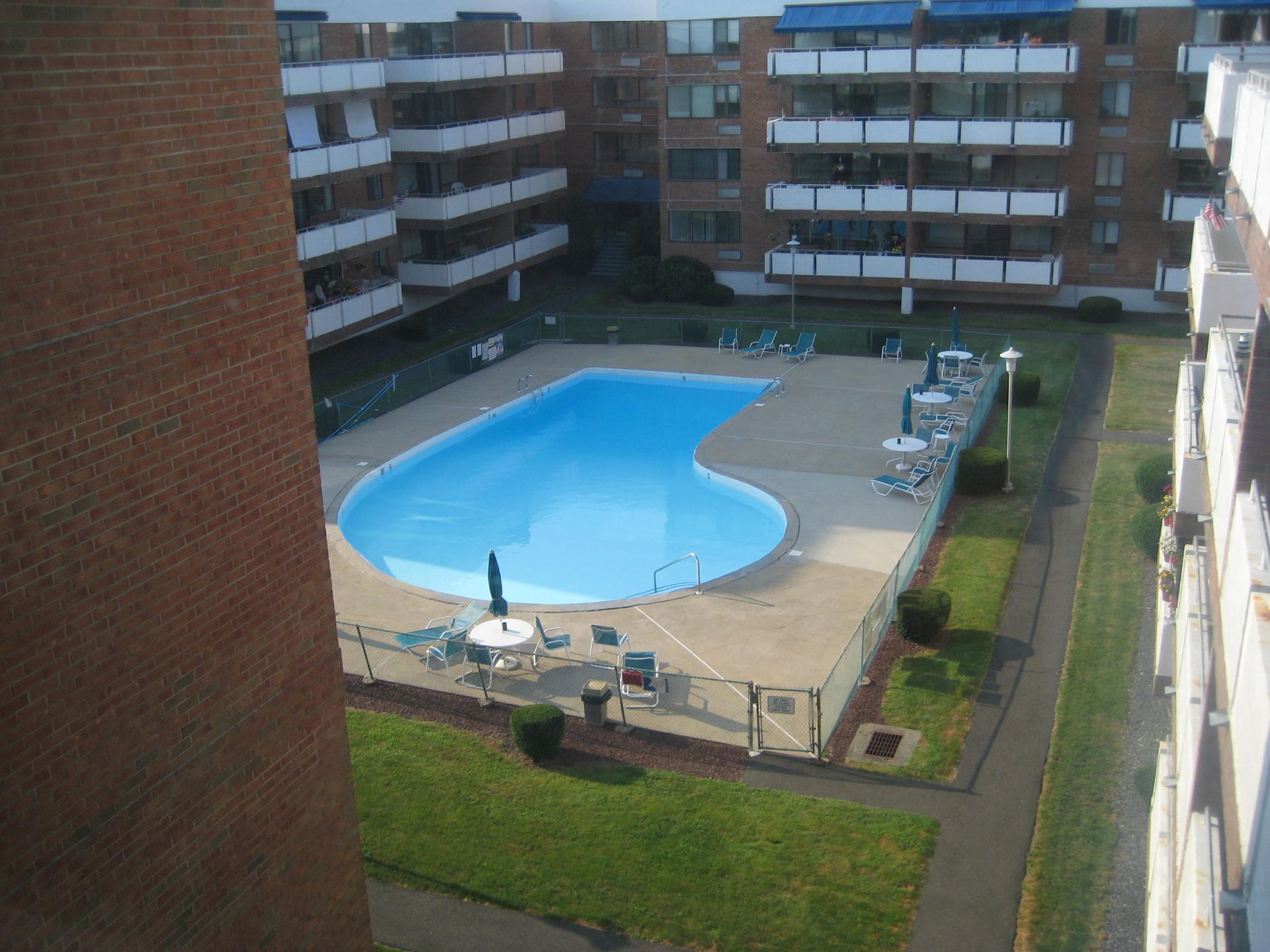 Apartment complex with a kidney-shaped pool.  Blue water, brick buildings, and surrounding grass.